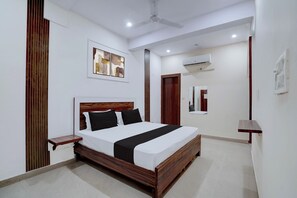 A modern hotel room with a wooden bed, a small bedside table, a ceiling fan, and an air conditioning unit. - Hotel O Sunrise (Ghaziabad)