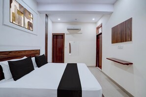 A hotel room with a bed, a wooden headboard, a painting, an air conditioning unit, a door, a wooden shelf, and a light switch. - Hotel O Sunrise (Ghaziabad)