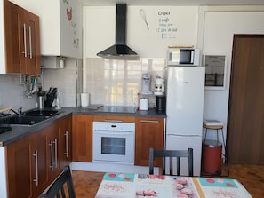 Cozinha com armários de madeira, micro-ondas, cafeteira e uma lixeira vermelha.