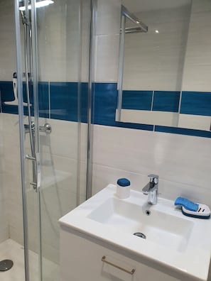 Casa de banho com cabine de duche em vidro, lavatório branco com dispensador de sabonete azul e espelho sobre o lavatório.