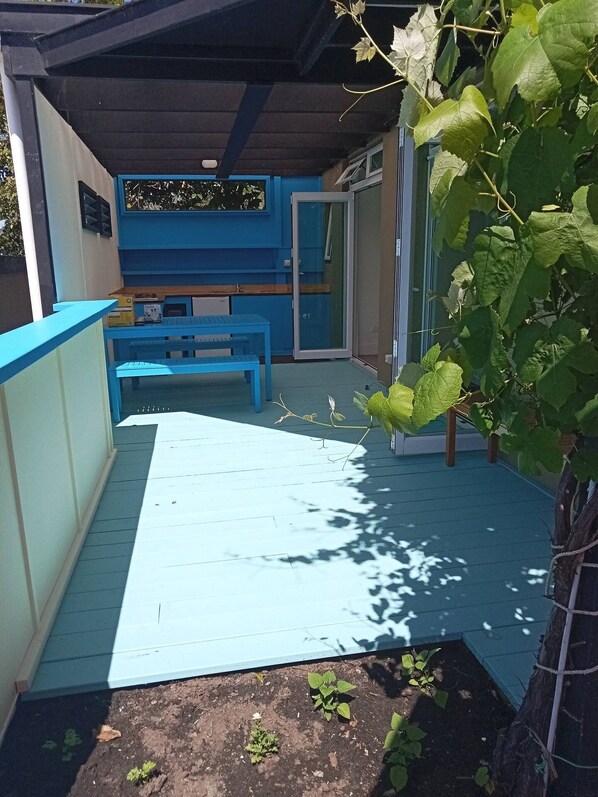 Un espace extérieur abrité comprenant un banc bleu, une table et une porte donnant accès à un espace intérieur.