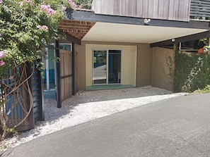 Un immeuble résidentiel doté d’un patio couvert, d’une entrée avec porte-fenêtre coulissante et d’une allée gravillonnée.