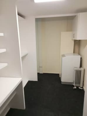 Un couloir étroit avec un radiateur blanc, une armoire blanche et une porte donnant sur une autre pièce.