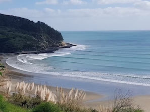 Un paysage côtier avec une plage de sable, de douces vagues et une colline boisée.