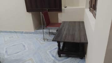 Una habitación pequeña con una mesa de madera oscura, una silla roja, una pared blanca y un suelo con diseño.