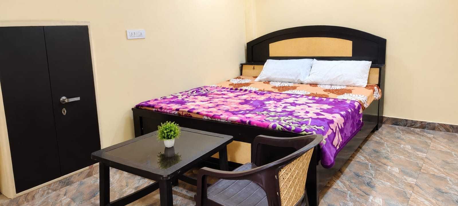 A single room with a bed, a small table with a plant, a chair, and a wardrobe.
