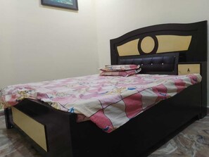 Un lit simple avec une couette, une table de chevet et une étagère fixée au mur.