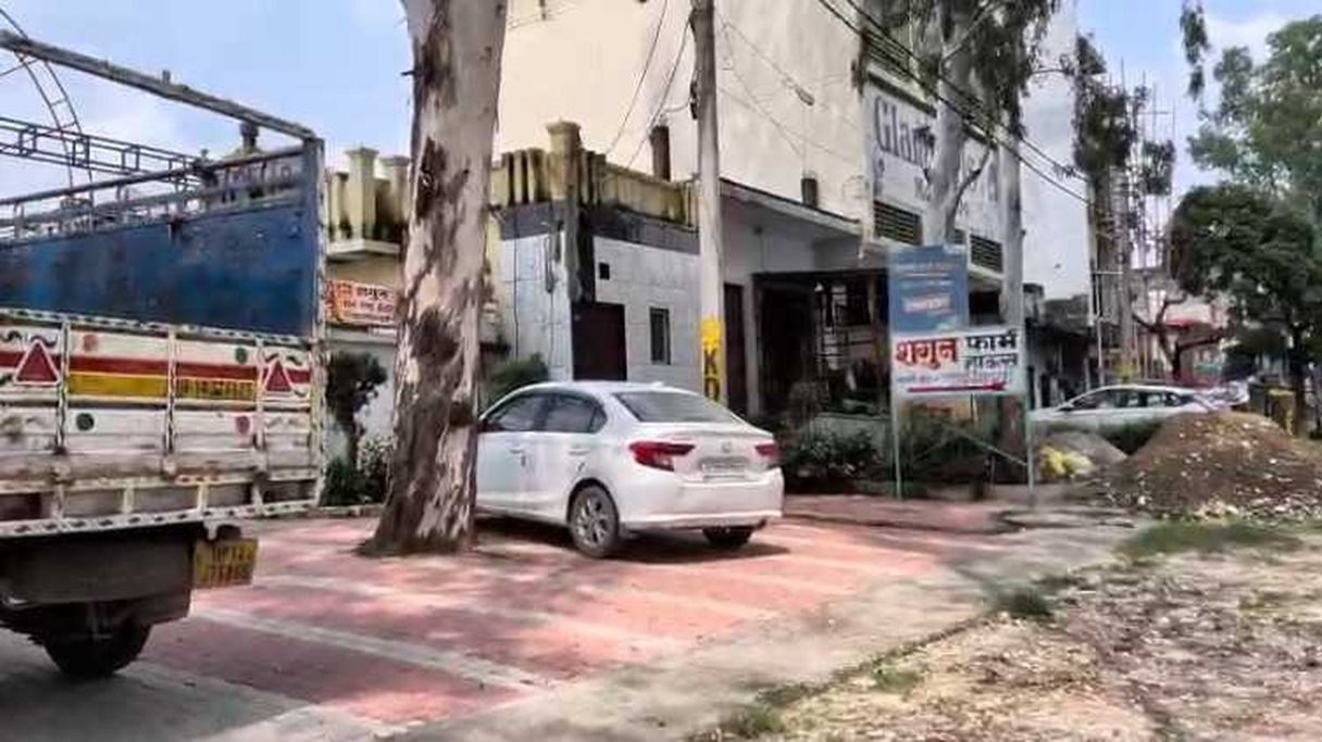Una calle con un coche blanco estacionado al borde, un camión azul al fondo y un edificio con un letrero en un idioma extranjero.