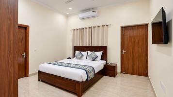 A bedroom with a bed, bedside tables, a ceiling fan, an air conditioning unit, and a TV mounted on the wall.