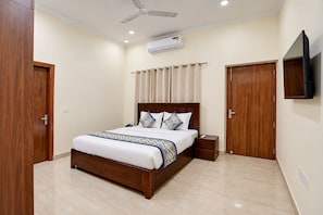 Une chambre à coucher comprenant un lit, des tables de chevet, un ventilateur de plafond, un appareil de climatisation et un téléviseur fixé au mur.
