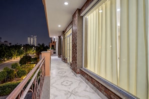 A balcony with a tiled floor, large windows, and a view of the cityscape at night. - Red Bricks By Carlton Suites  (Noida)