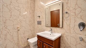 A bathroom with a marble wall, a sink, a mirror, a toilet, and a shower.