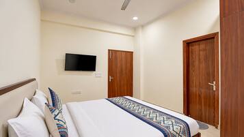 A hotel room with a bed, a television mounted on the wall, and two wooden doors.