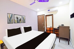 Una habitación de hotel con una cama, un escritorio, una silla, un armario y un ventilador de techo.