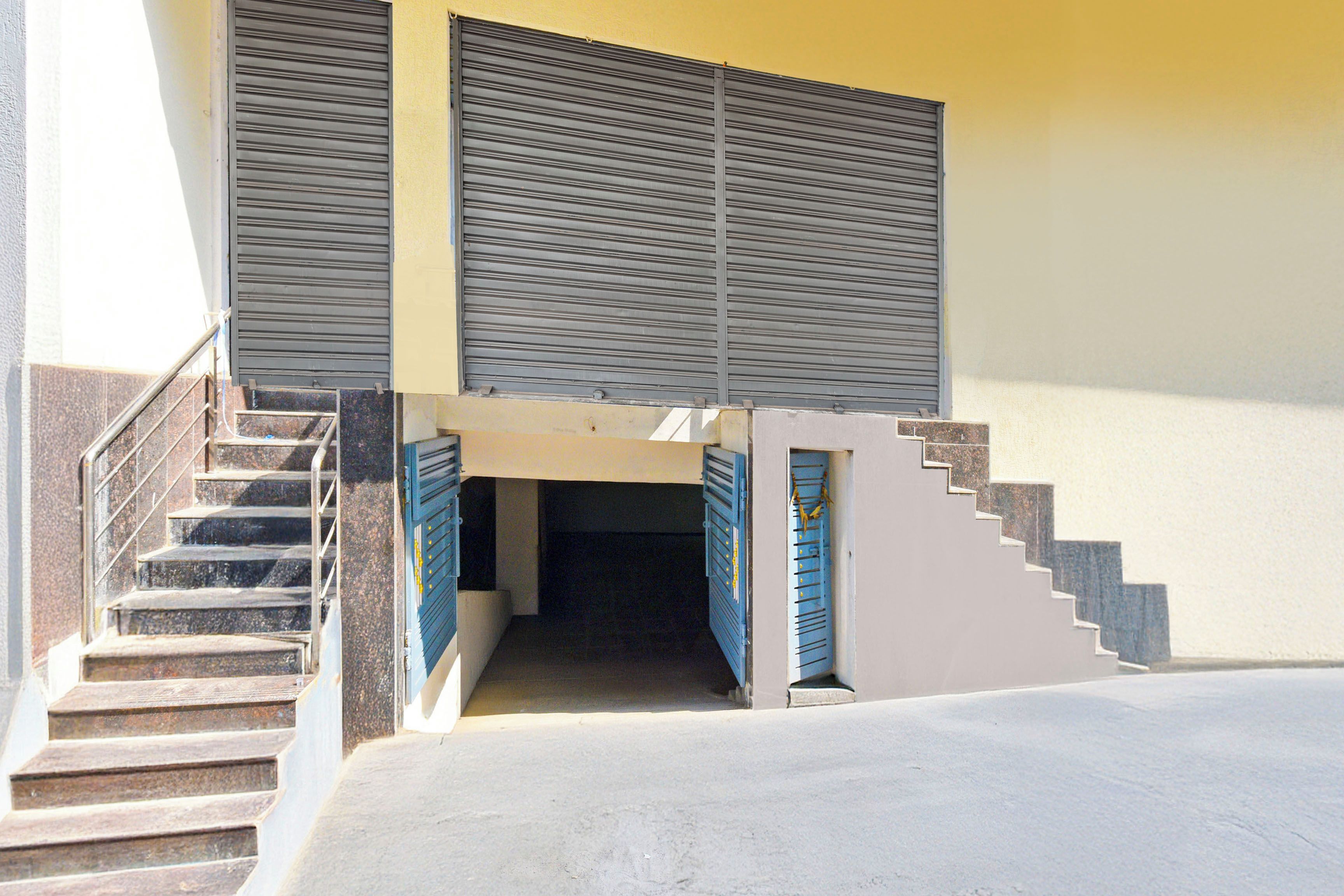 Un edificio con una escalera que conduce a una puerta con un cerrojo azul, barandilla de metal y piso de concreto.