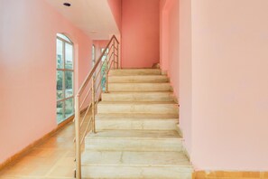 A staircase with a metal railing leading to a landing, surrounded by pink walls and a large window.