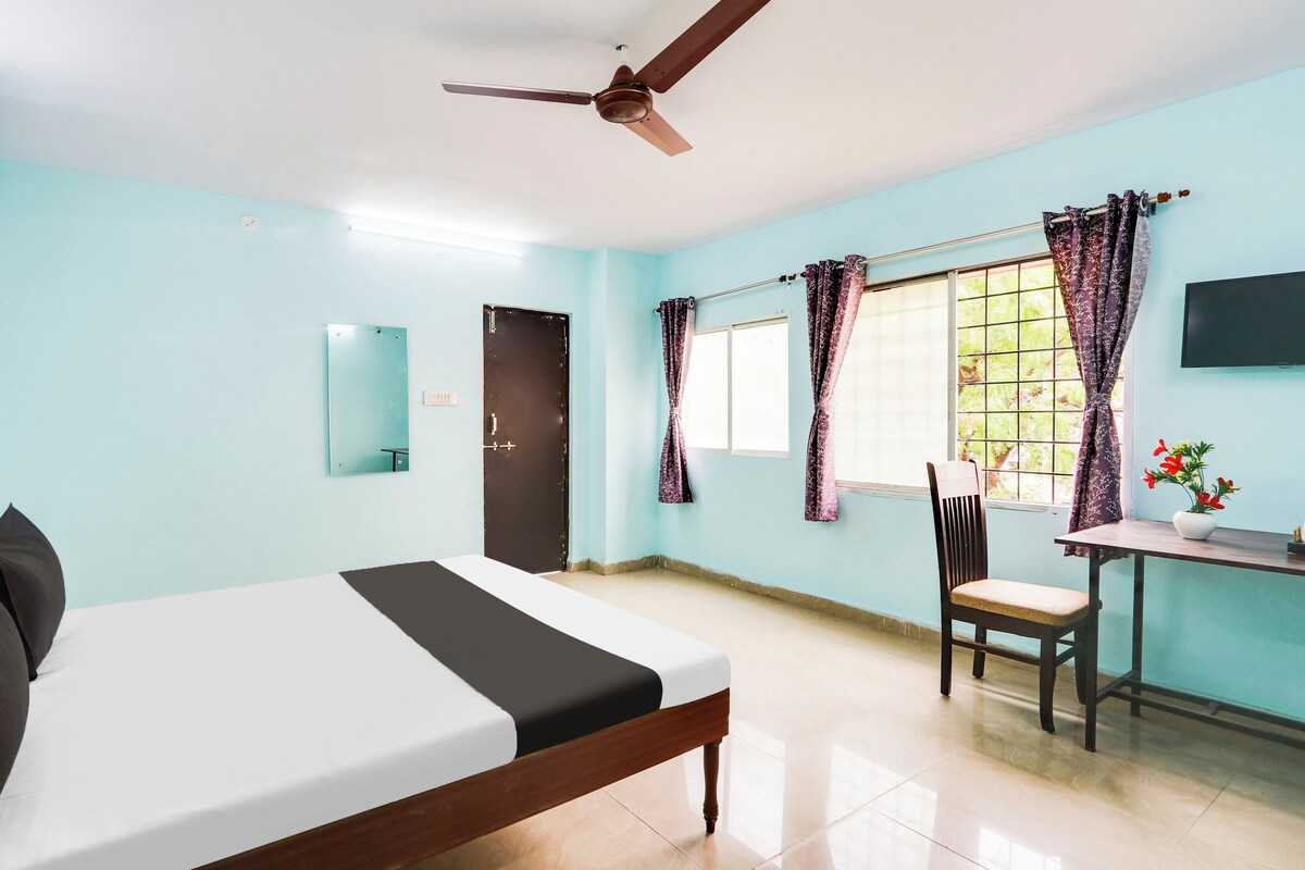 Una habitación con cama, escritorio, silla, televisión y ventana con cortinas.