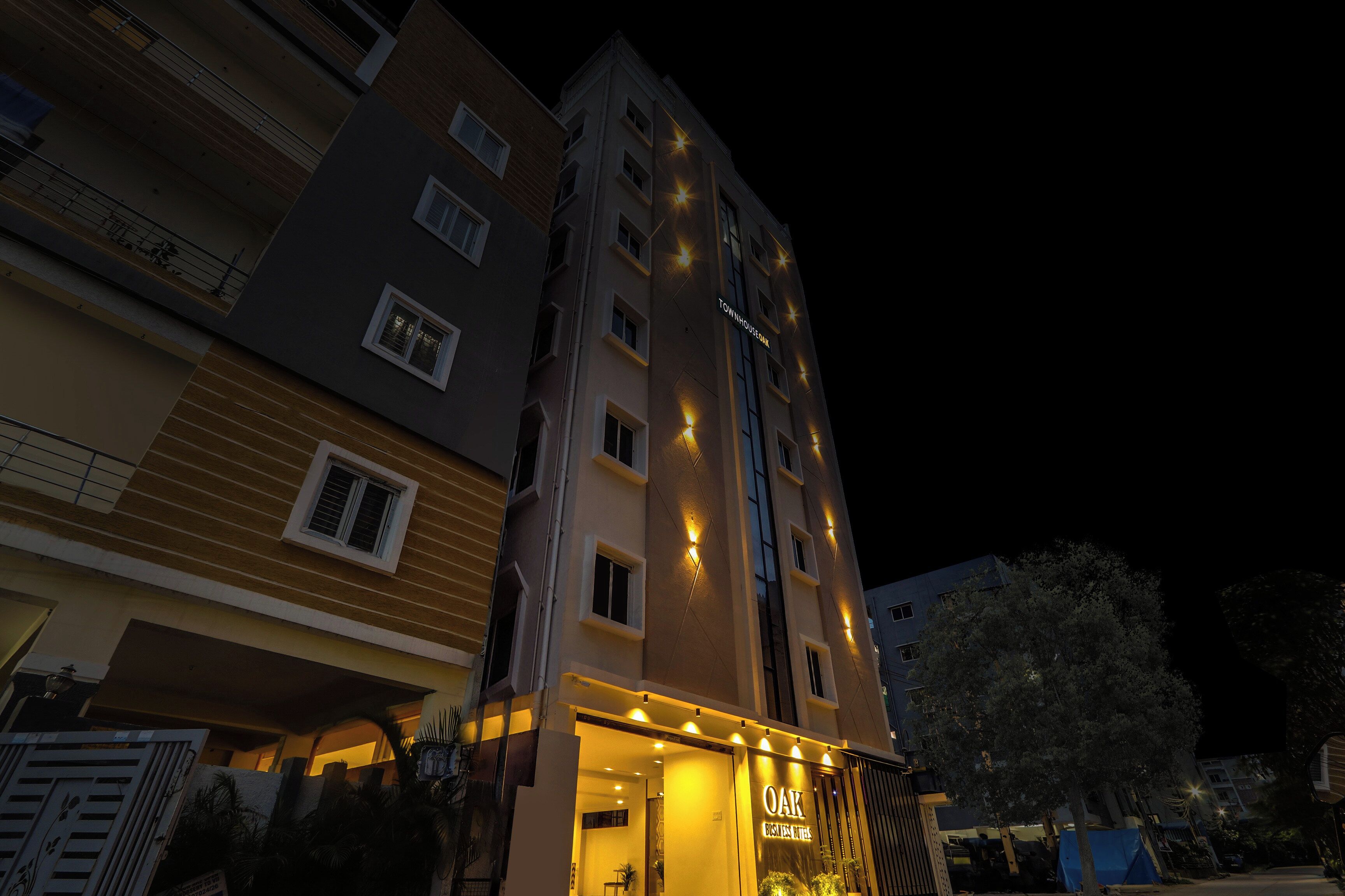 Un immeuble à plusieurs étages, doté d’une enseigne lumineuse indiquant « TOWNHOUSE DAK » et « OAK BUSINESS HOTELS ».