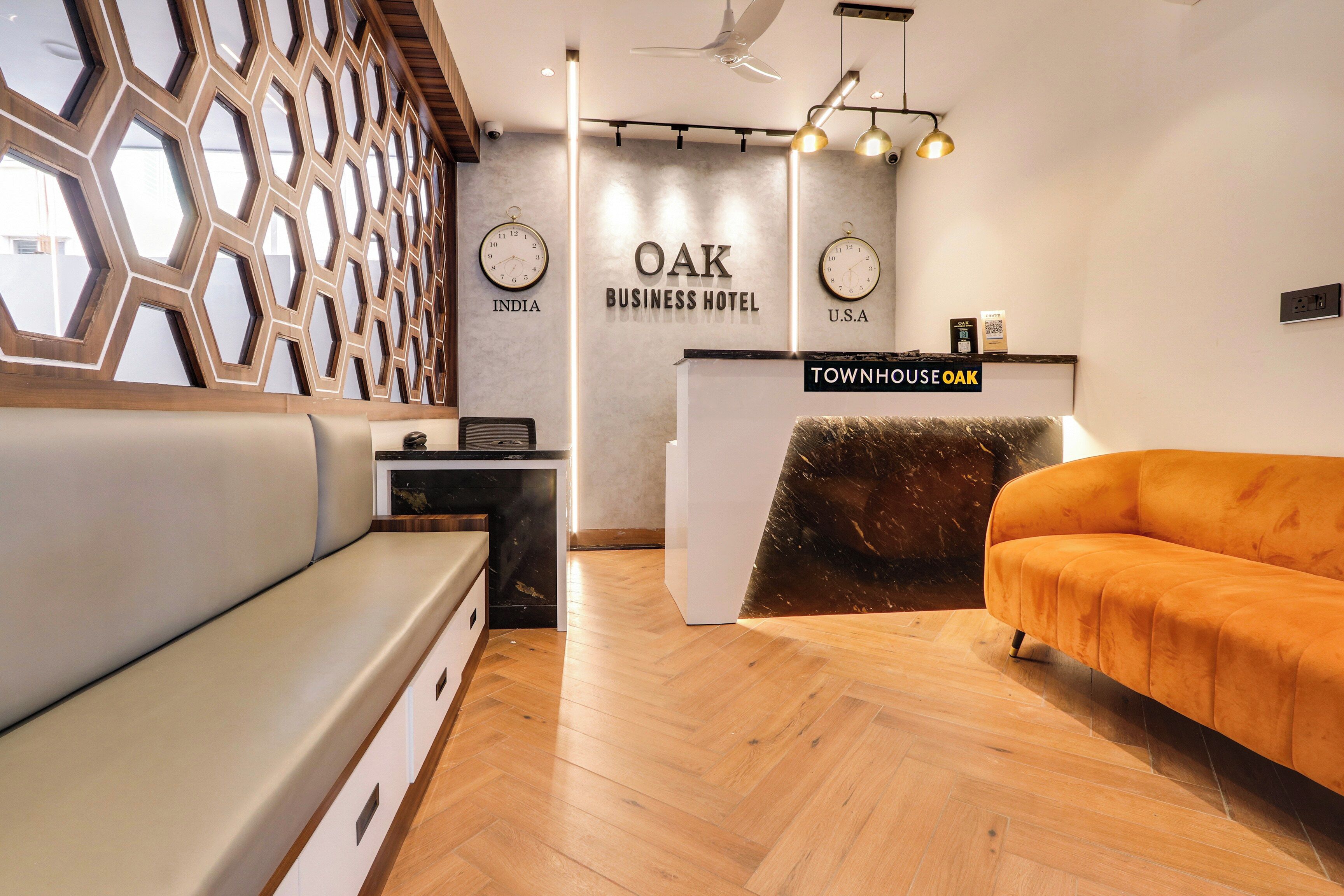 Un espace d’accueil moderne, avec un comptoir en bois, un canapé et un mur orné d’horloges indiquant différents fuseaux horaires.