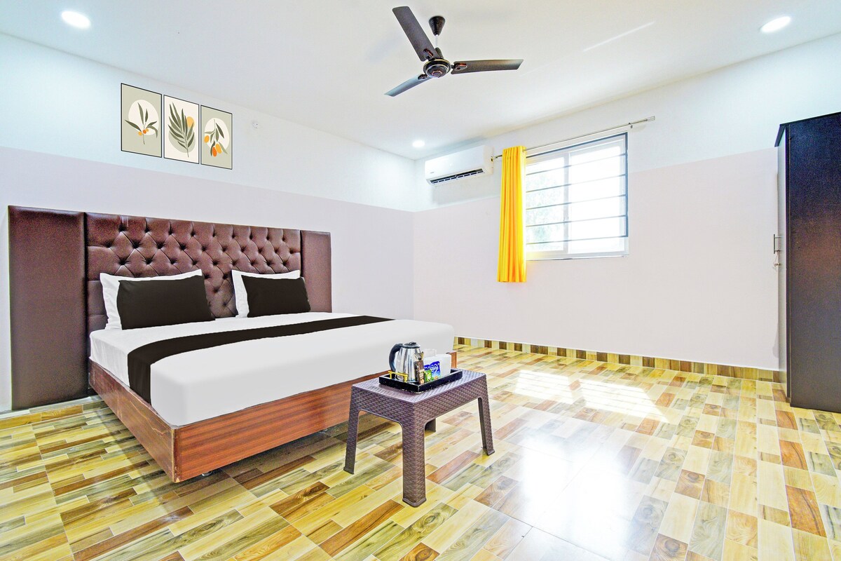 Une chambre d’hôtel avec un lit, une petite table avec une bouilloire, un ventilateur de plafond, un appareil de climatisation et une fenêtre avec des rideaux.