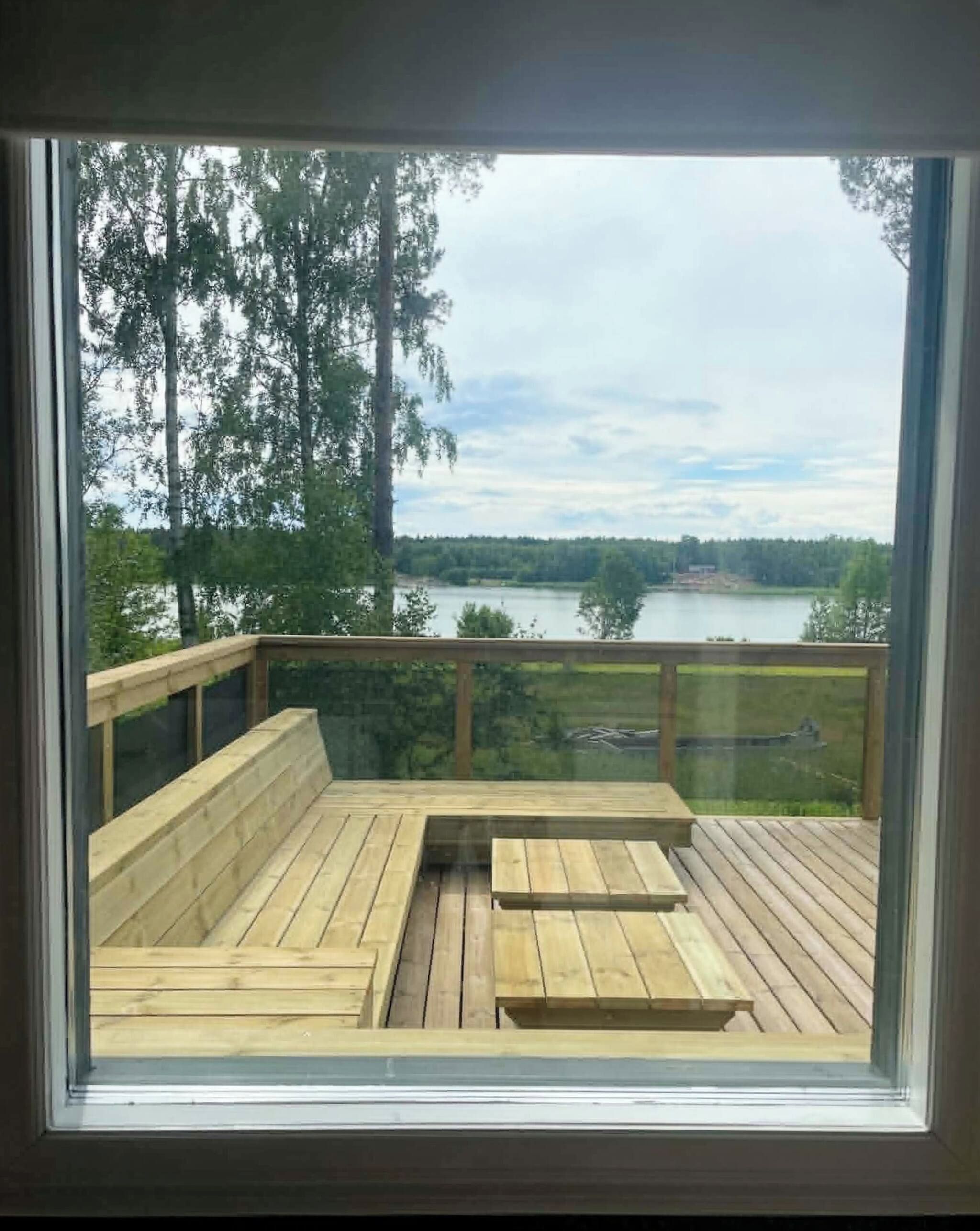 A deck with a wooden floor and a bench, overlooking a lake with trees and a cloudy sky.