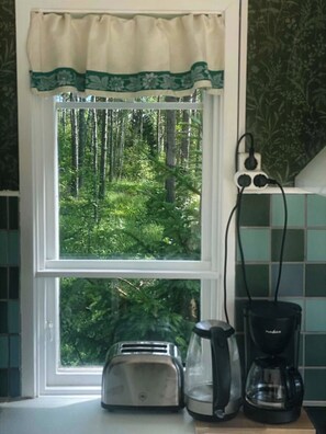 A kitchen with a window overlooking a forest, a toaster, and a coffee maker on the counter.