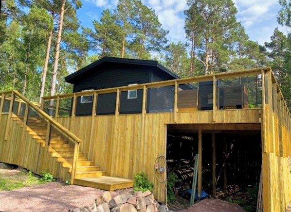 A two-story wooden cabin with a staircase leading to a deck, surrounded by trees.