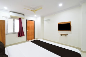 A hotel room with a bed, a ceiling fan, a window with curtains, a door, a mounted TV, and a shelf. - Hotel O Brundavan Residency (Hyderabad)