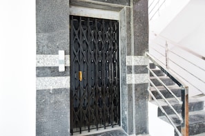 A black metal gate with a diamond pattern, set in a stone wall with white and gray tiles. - Hotel O Brundavan Residency (Hyderabad)