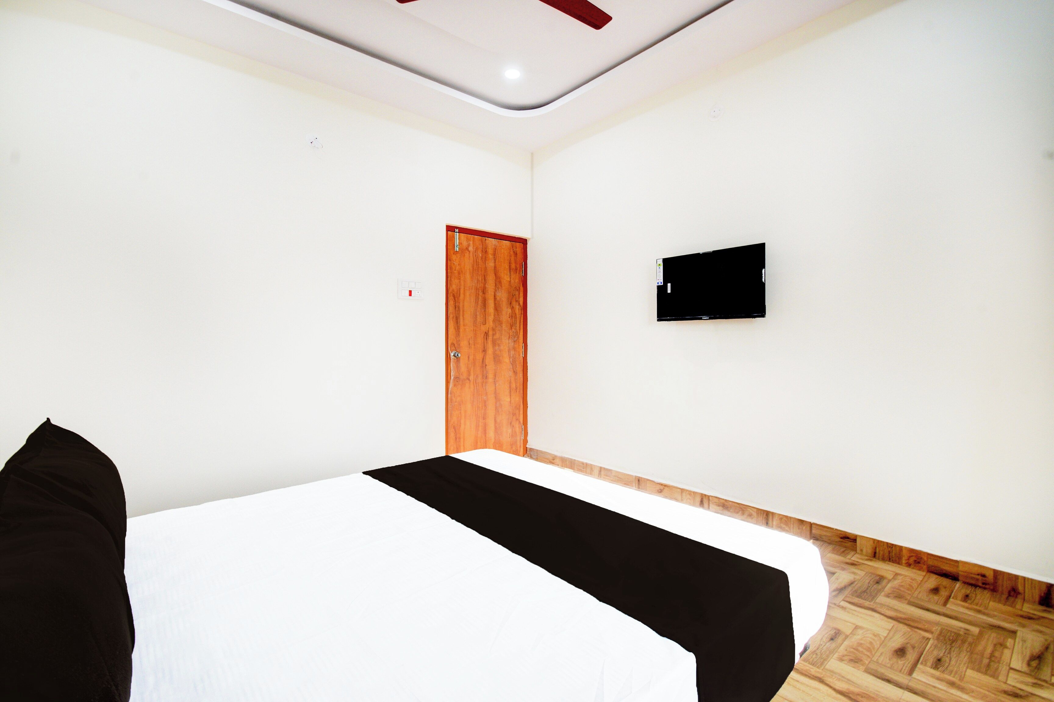 A hotel room with a bed, a television mounted on the wall, and a wooden door.