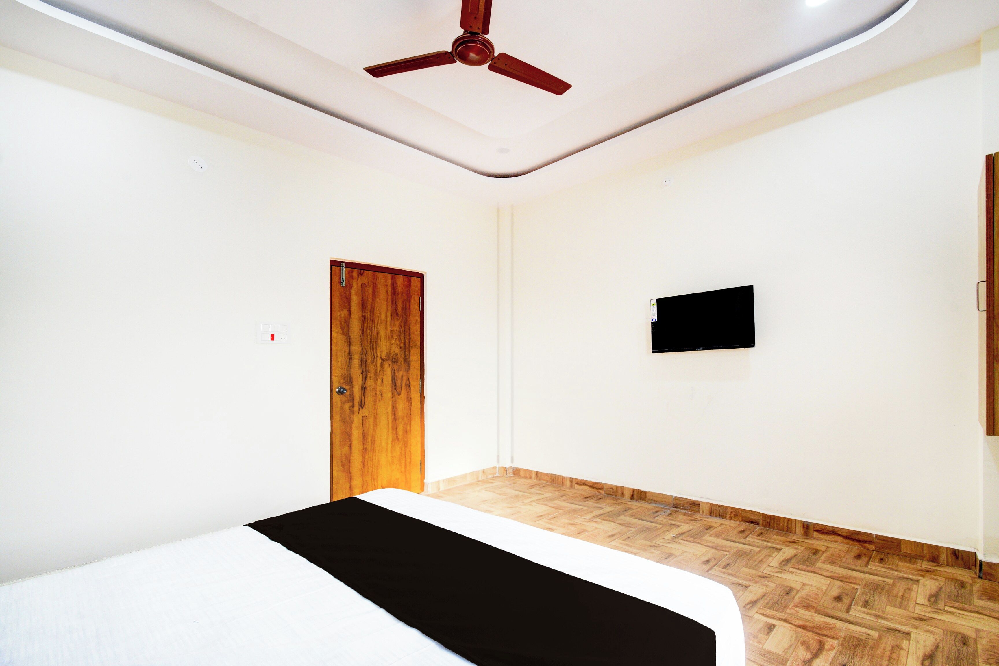 A room with a bed, a ceiling fan, a wooden door, and a mounted television.