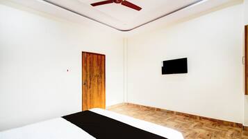 A room with a bed, a ceiling fan, a wooden door, and a mounted television.