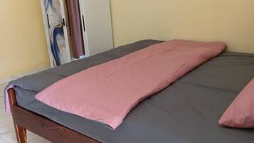 Una cama con colchón gris y ropa de cama rosa, un cabecero de madera y un armario con diseño de mármol.
