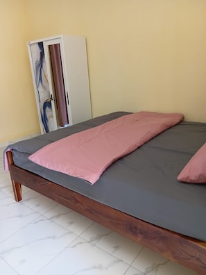 A bed with a grey mattress and pink bedding, a wooden headboard, and a wardrobe with a marble design. - Christian Homestay (Labuan Bajo)