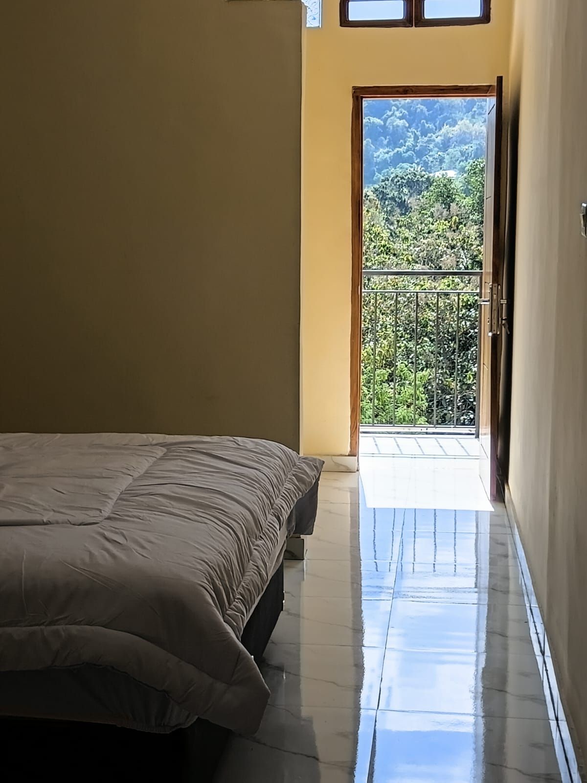 Un dormitorio con una cama, una puerta que da a un balcón y vistas al exterior con vegetación.