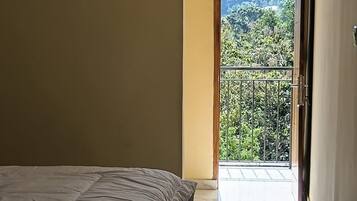 Un dormitorio con una cama, una puerta que da a un balcón y vistas al exterior con vegetación.