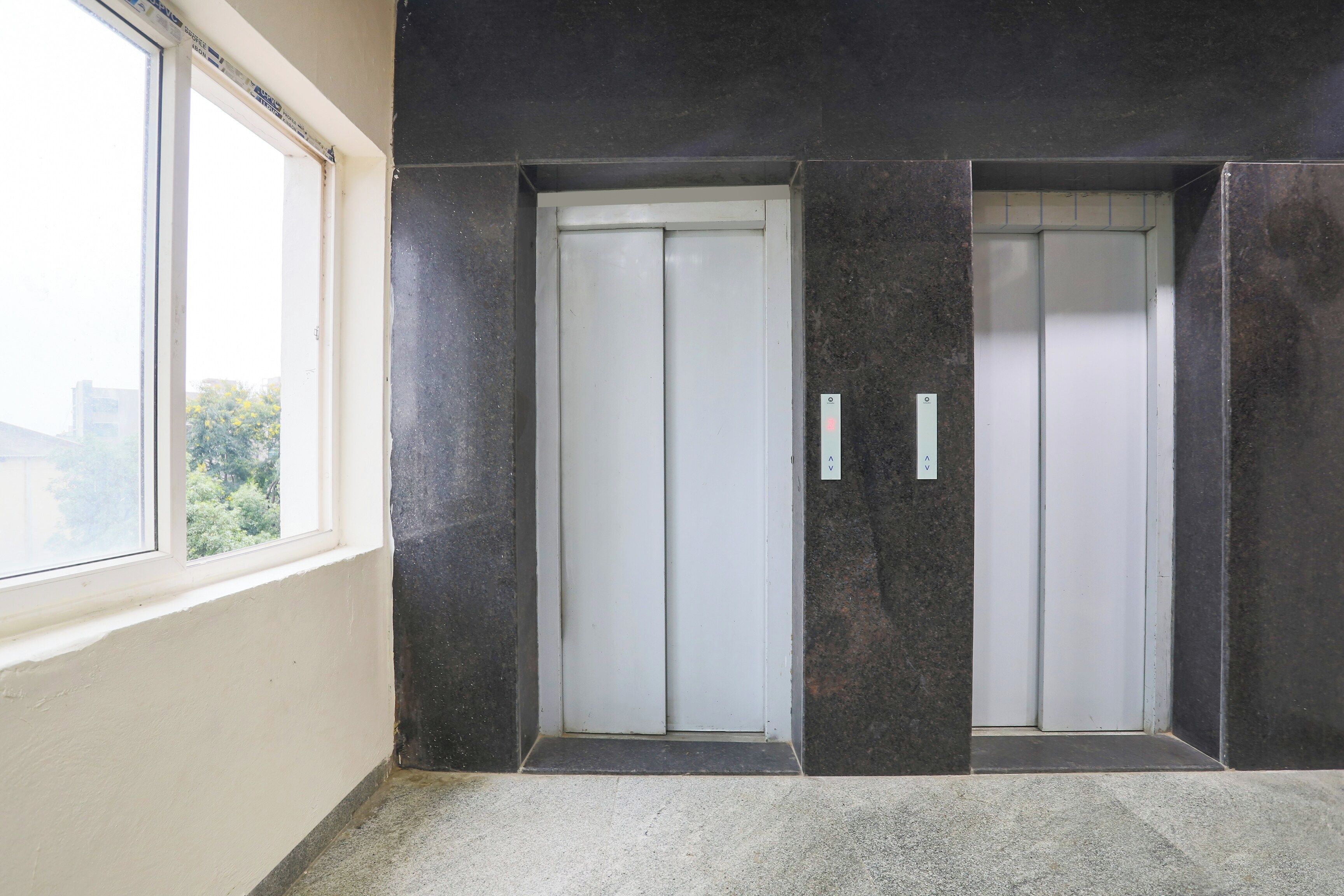 A pair of elevator doors with a control panel, a window, and a concrete floor.