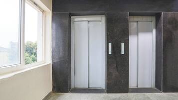A pair of elevator doors with a control panel, a window, and a concrete floor.