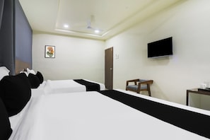 A hotel room with a bed, a desk, a chair, a television, and a ceiling fan. - Townhouse RIO (Ramachandrapuram)
