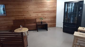 Een kamer met houten lambrisering, een houten bank, een tafeltje met een bloempot, een ronde tafel en een zwarte automaat.