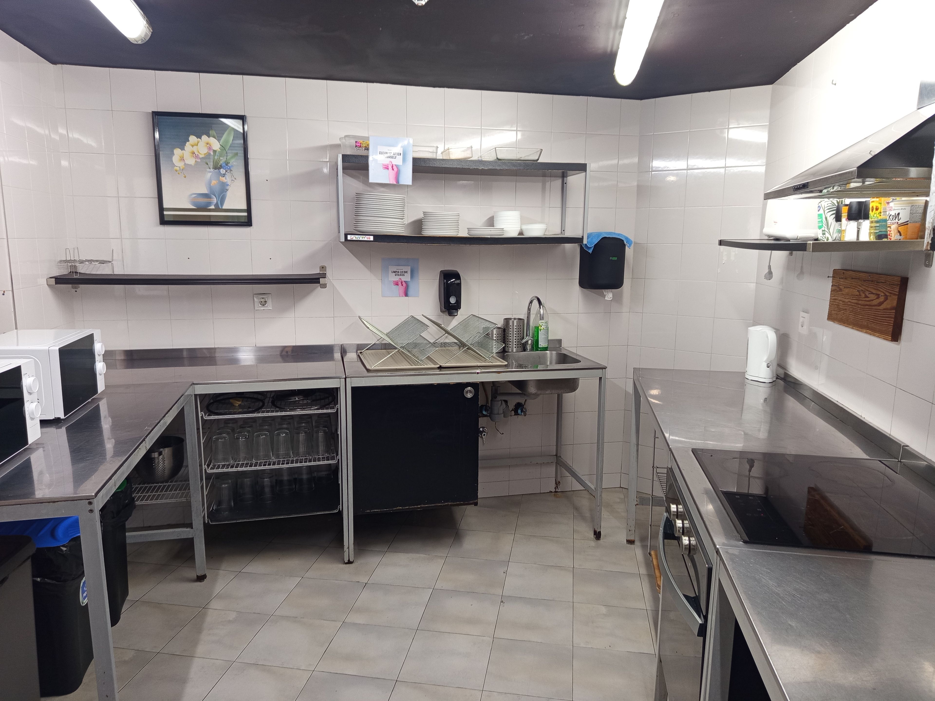 Una cocina comercial con electrodomésticos de acero inoxidable, un salpicadero de azulejos y un estante empotrado con utensilios de cocina.