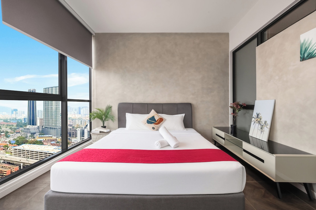 Una habitación de hotel moderna con una cama grande, vistas a la ciudad, una mesita de noche y una mesilla.
