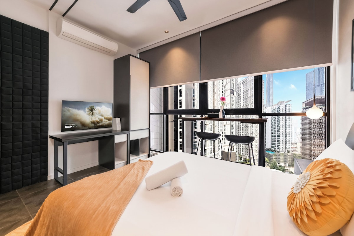 Una habitación de hotel moderna con una cama grande, un escritorio con televisión de pantalla plana, un balcón con vistas a la ciudad y un ventanal amplio.