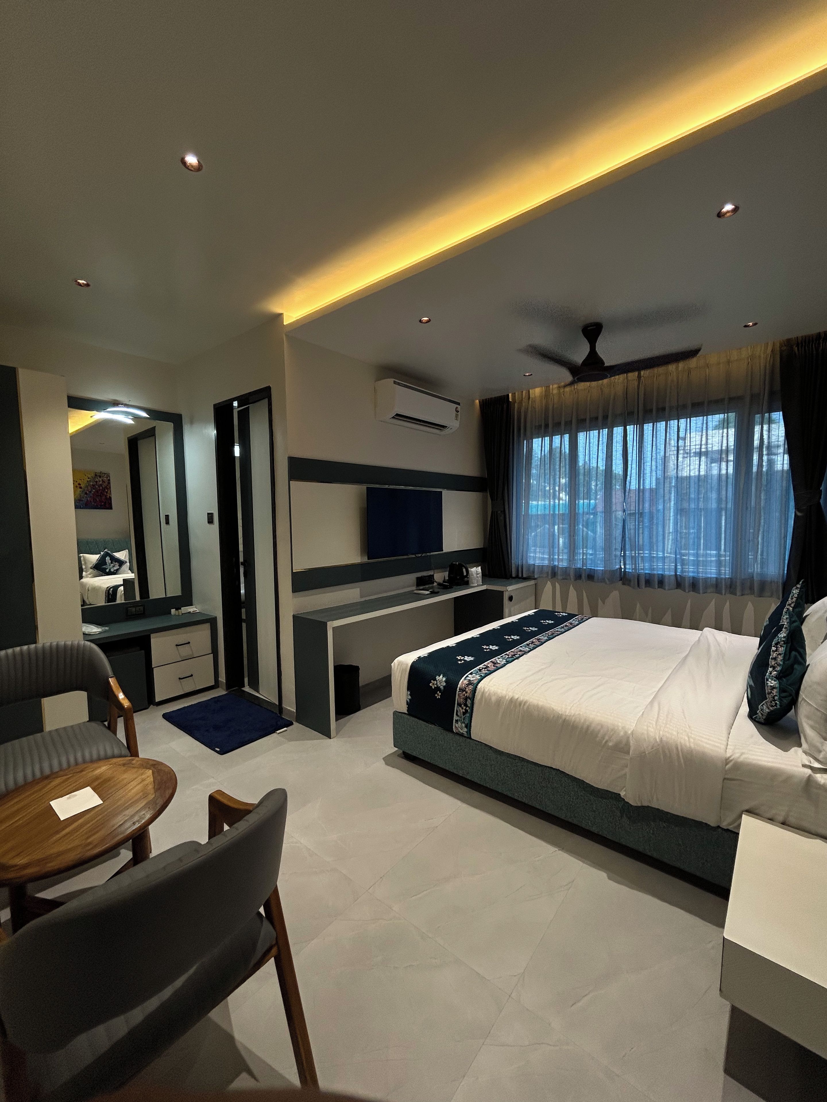 A modern hotel room with a bed, desk, chair, and a large window with curtains.