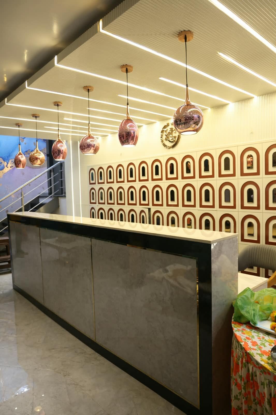 Una zona de recepción con mostrador de mármol, luces colgantes y un revestimiento de pared con diseño.