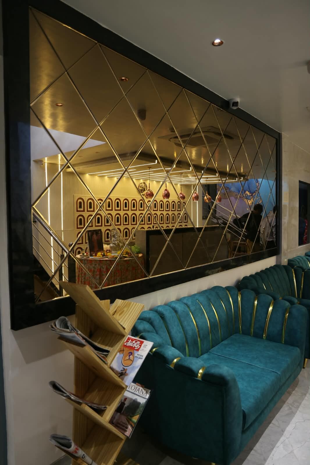 A modern interior with a teal sofa, a wooden side table with magazines, and a decorative wall with geometric patterns.