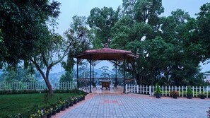 A gazebo with a tiled roof, surrounded by a white picket fence, set in a landscaped garden with potted plants and trees. - Miln Town by Zari (Coonoor)