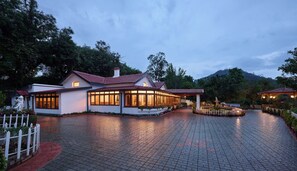 A two-story building with a red-tiled roof, large windows, and a paved driveway. - Miln Town by Zari (Coonoor)