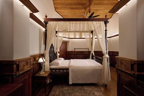 A four-poster canopy bed with a wooden headboard, a nightstand with a lamp, and a patterned rug on the floor. - Miln Town by Zari (Coonoor)