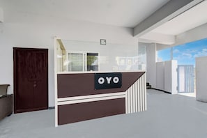 A reception desk with a sign reading 'OYO' in a modern interior with white walls and a large window. - Hotel O RRR Residency & Luxury rooms (Hyderabad)